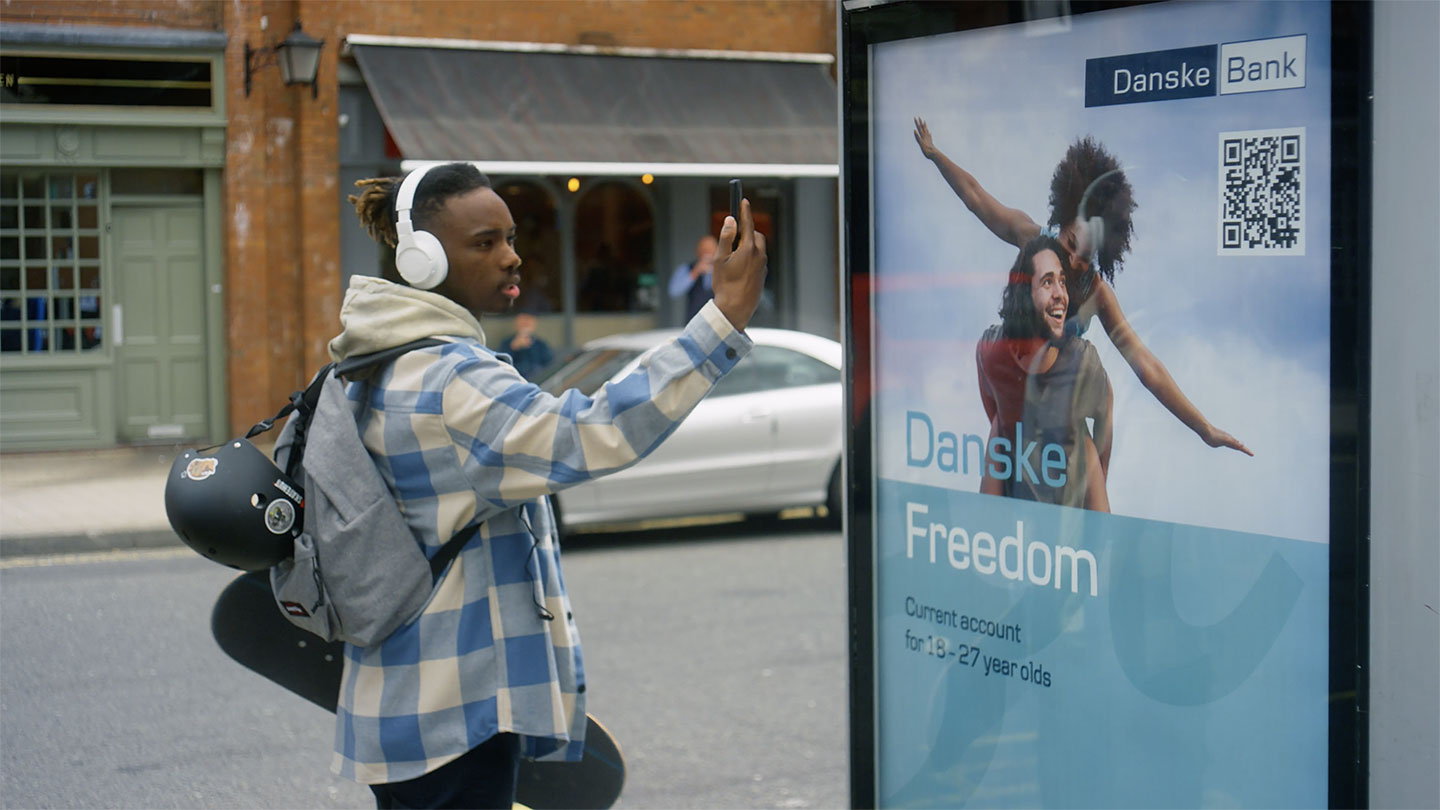 Young man photographing QR code on outdoor sign