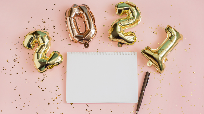 A pink bacground, with gold balloons spelling out '2020' and a blank piece of paper and pen.