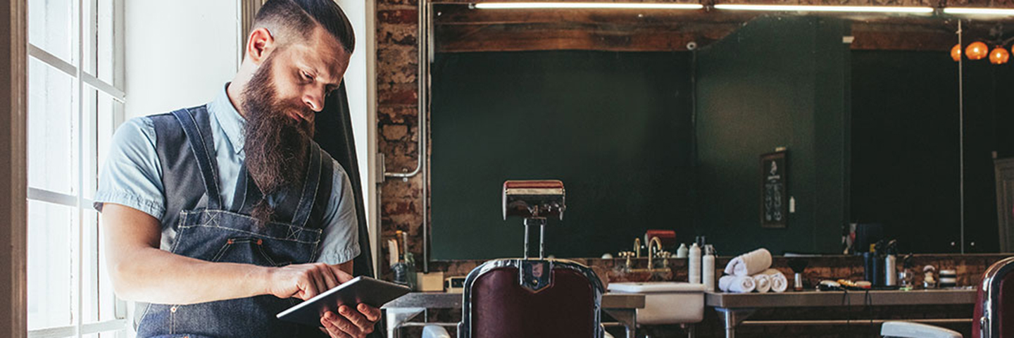 Barber sitting in hair salon using tablet device