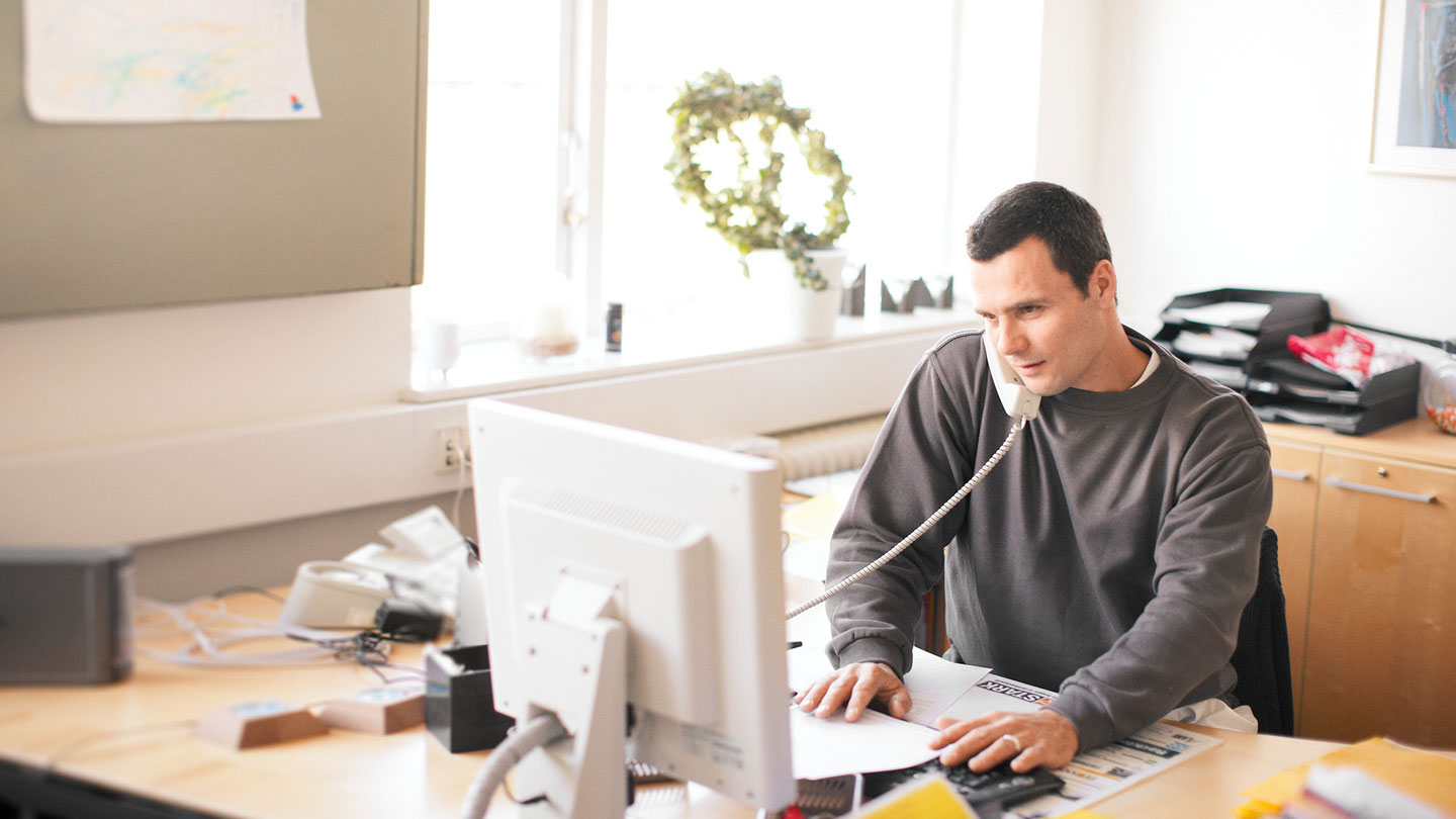 Man working on computer whilst using phone