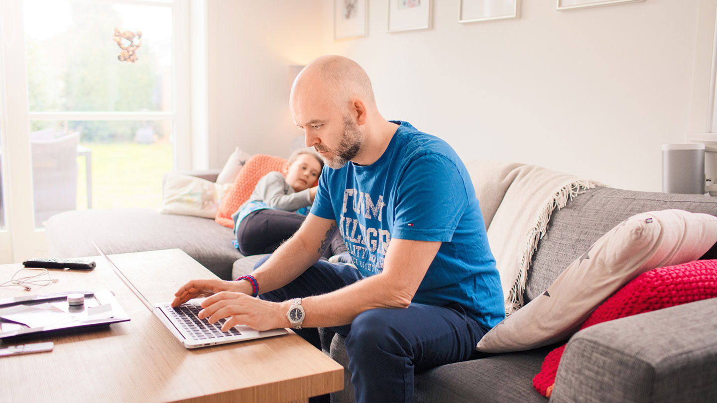 Man using laptop in livingroom with child in background