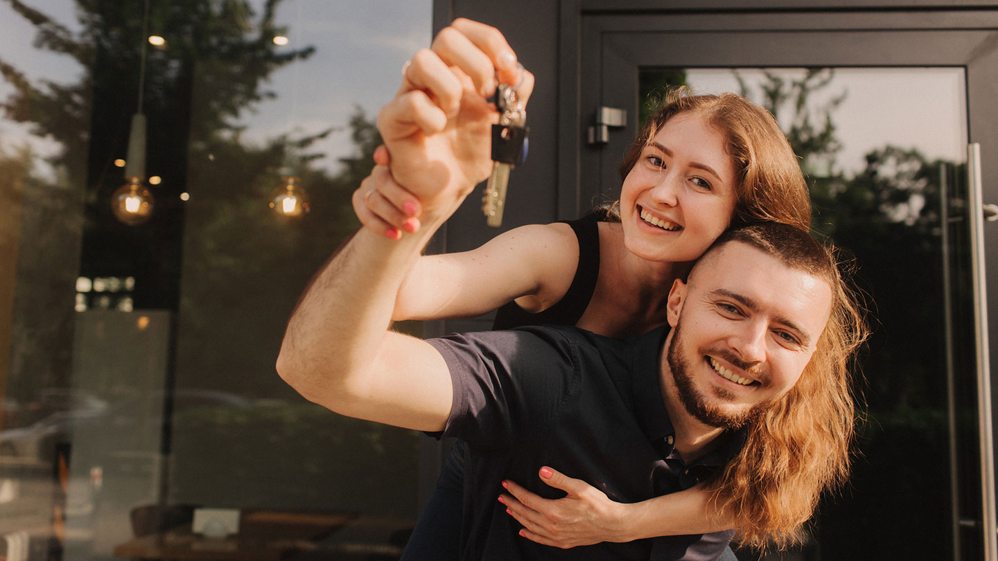 A joyful moment outside a modern building, with couple holding up a set of keys symbolising new homeownership or achievement.