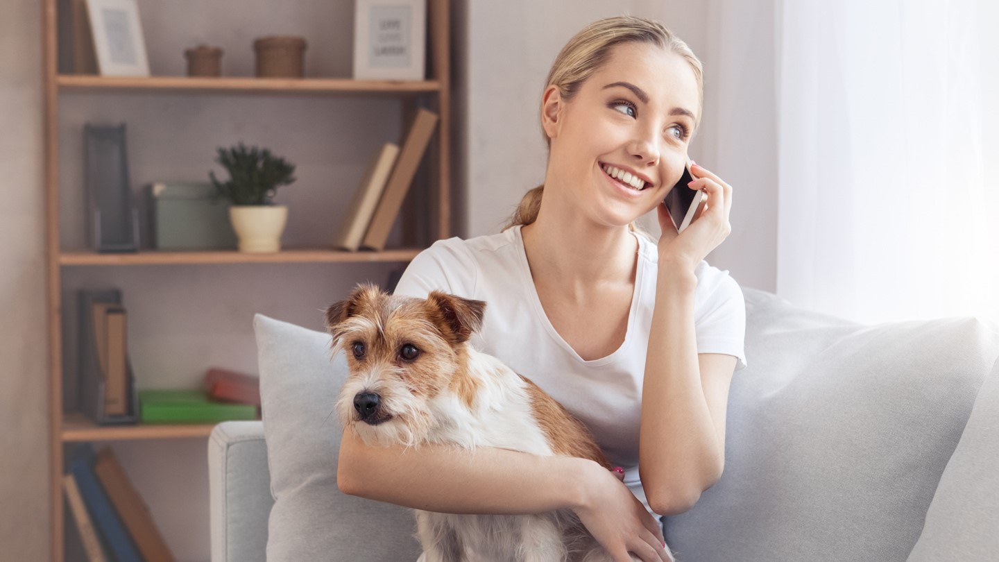 Woman smiling on phone whilst holding a dog