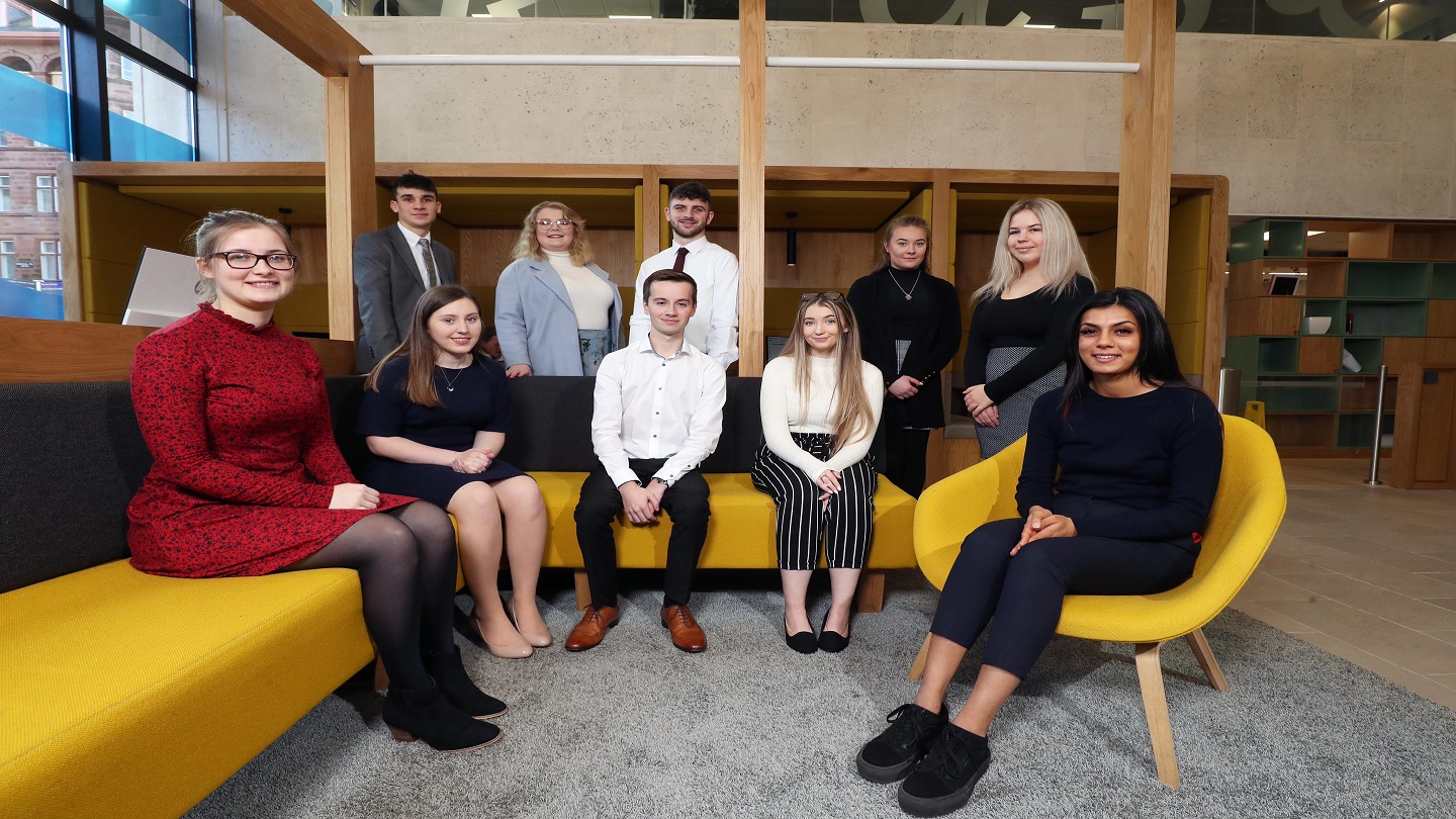 Ten people sitting and standing inside a Danske Bank branch. They are all smiling and looking at the camera.