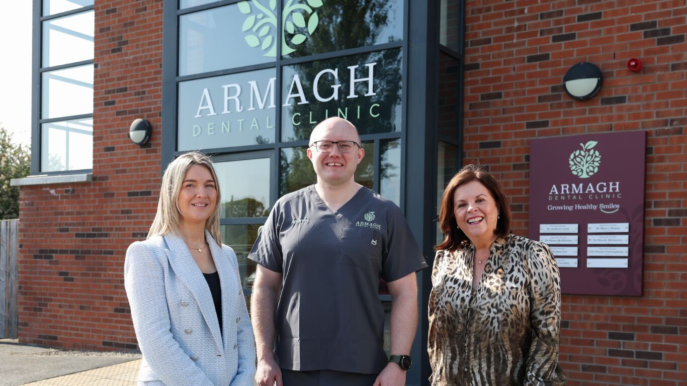 Three people standing together outside of Armagh Dental Clinic, smiling.