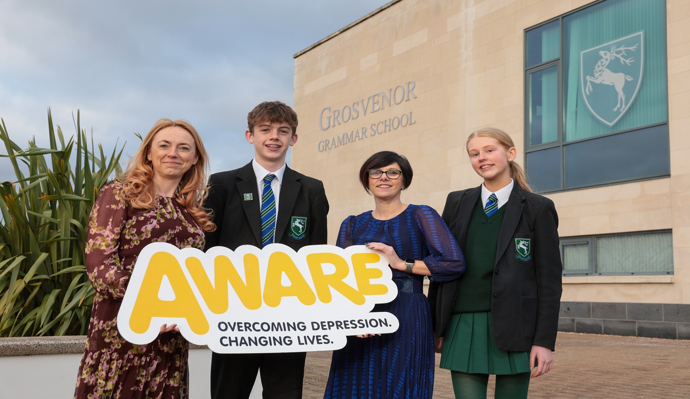 Four people stand outside a school holding an AWARE NI sign.