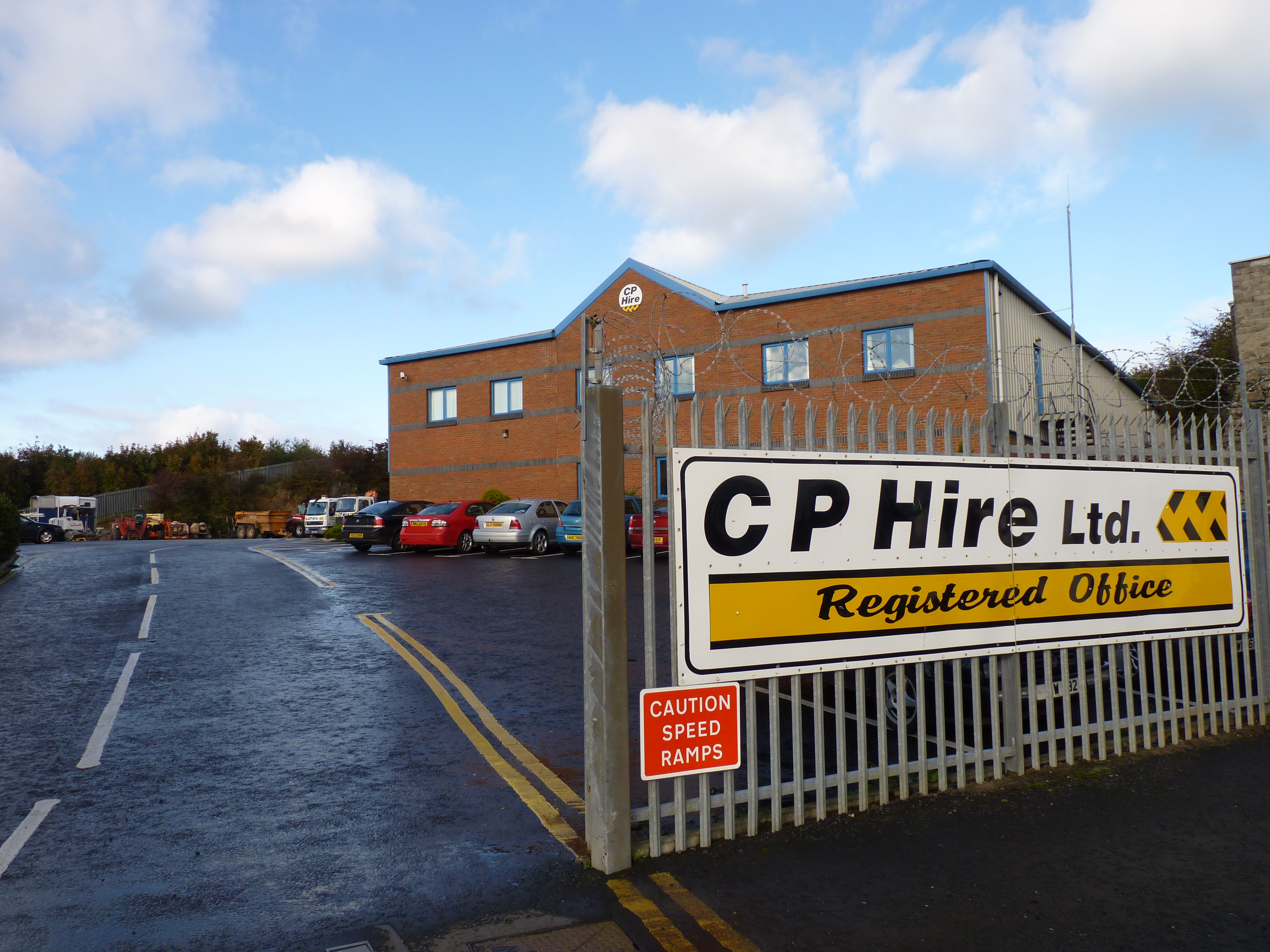 Photo taken outside a CP Hire Ltd. office building. Shows a road in, cars parked in front of an office and a large sign that says 'CP Hire Ltd'.