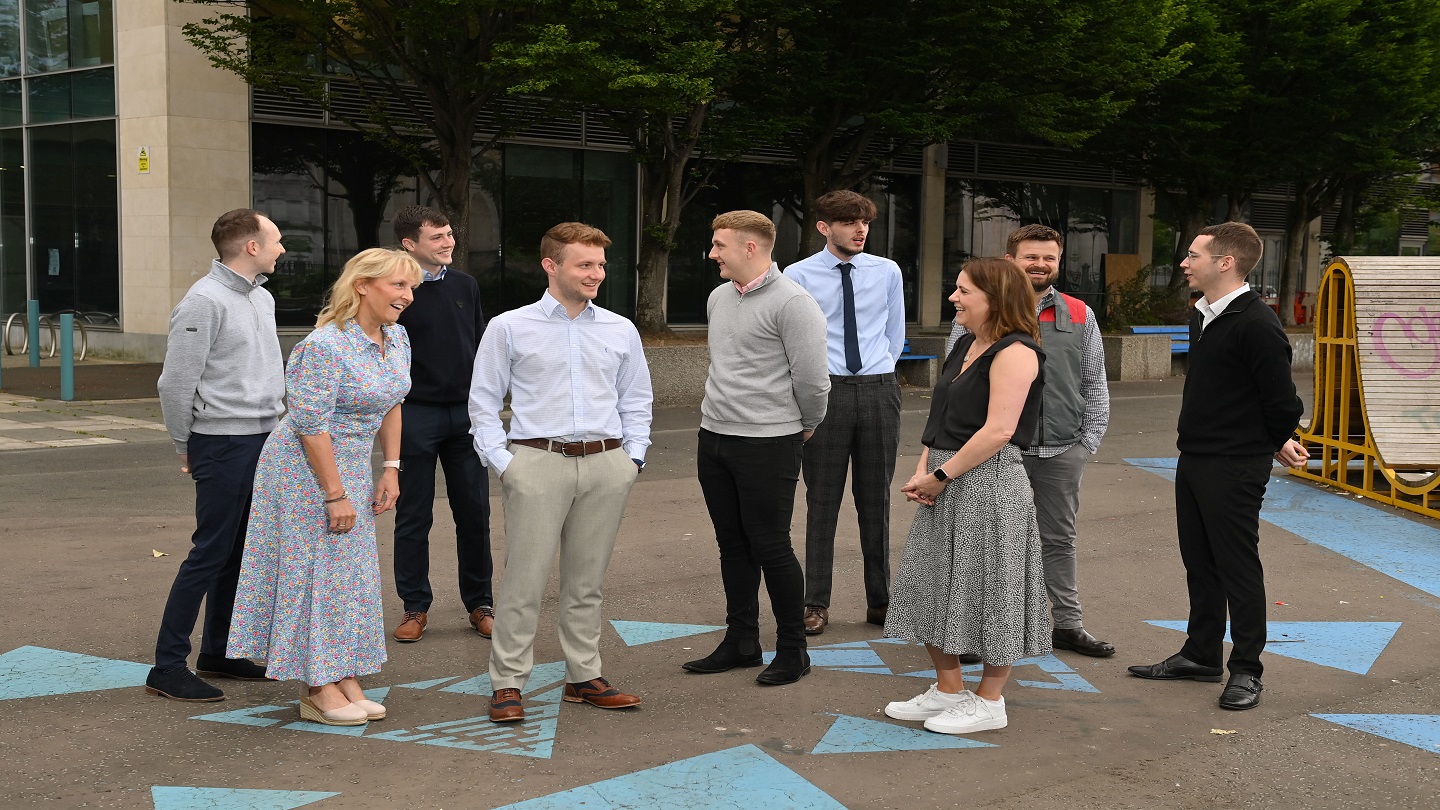 A group of nine people stand outside chatting to each other.
