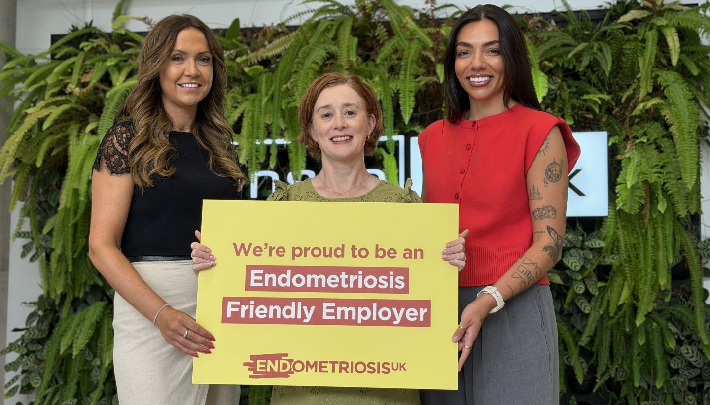 "Three Danske colleagues smiling at the camera while holding a prop that says 'we're proud to be an endometriosis friendly employer'"