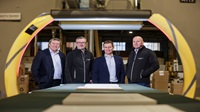Exorna, part of the Oliver Exorna Group, invests in major solar panel project with support from Danske Bank Four people stand inside a warehouse behind equipment.