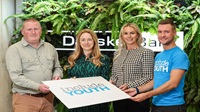 Danske Bank announces new charity partnership with Include Youth Four people stand together in a Danske Bank branch holding a sign that has the Include Youth logo on it.