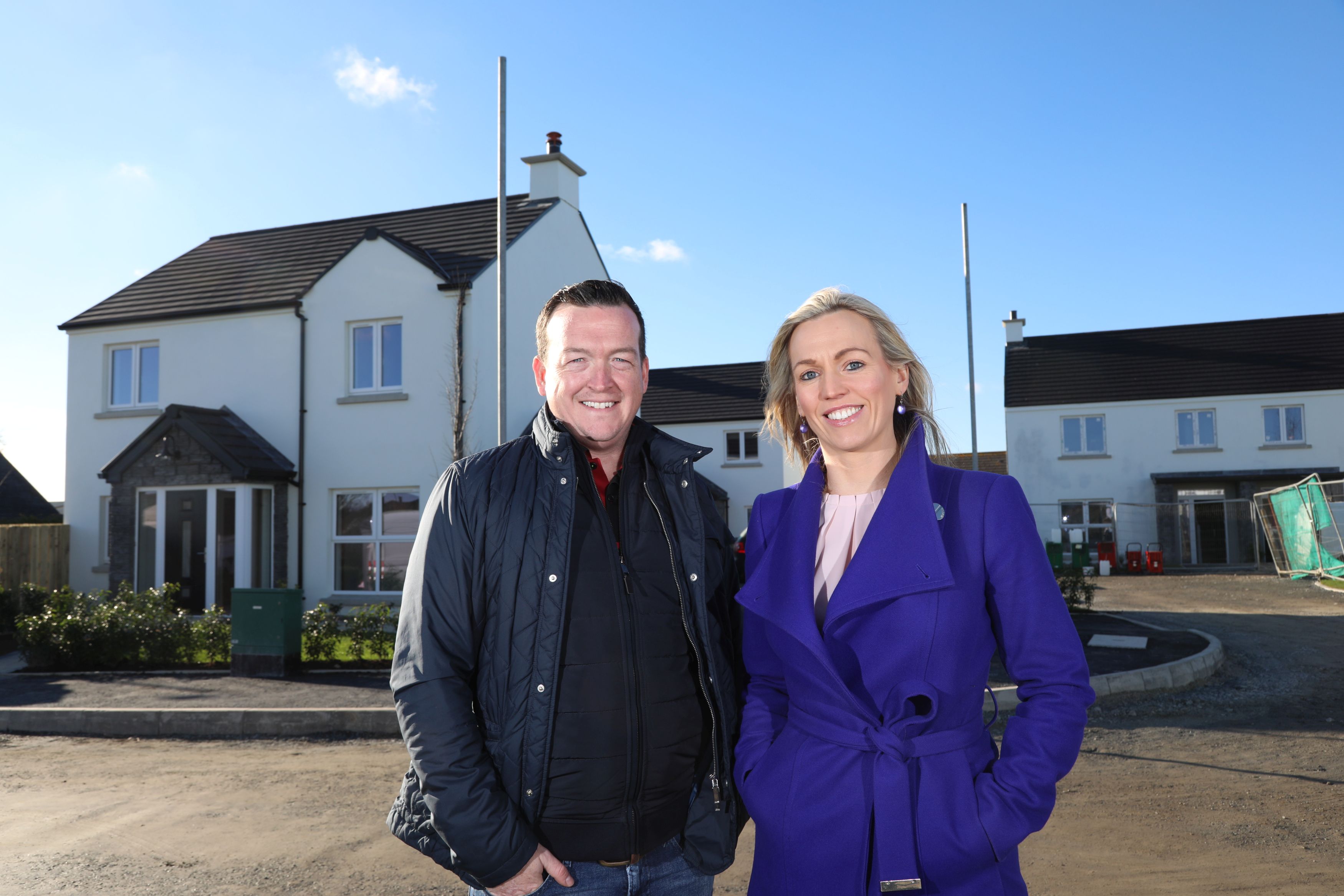 A man and woman stand outside, in front of some houses.