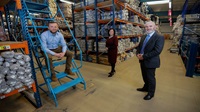 Three people inside a large warehouse, surrounded by rugs and carpets.