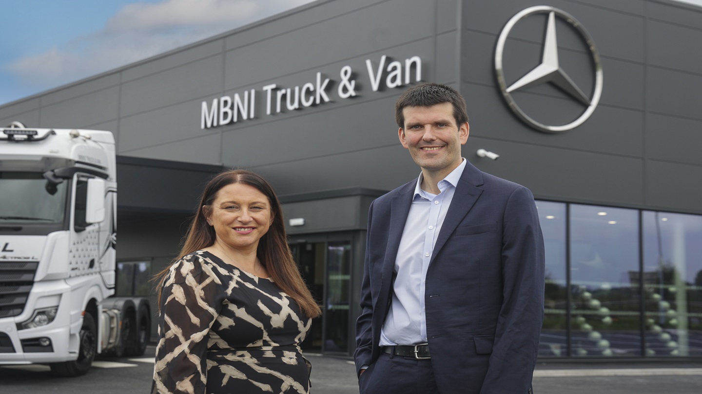 A woman and man stand outside a large Mercedes-Benz NI (MBNI) Truck and Van showroom