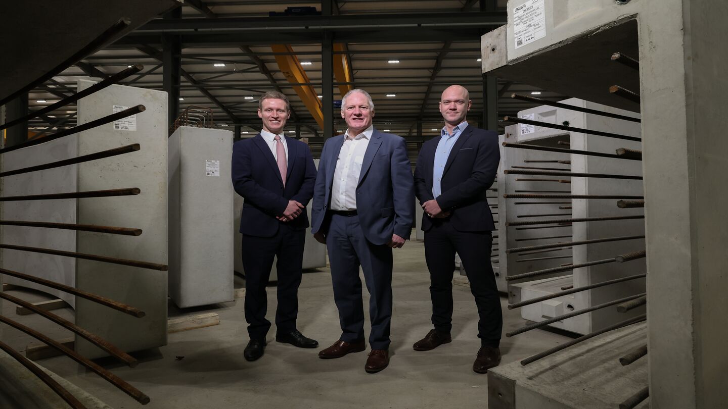 Three men stand inside a concrete manufacturer factory.