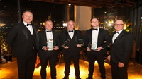 Five men stand together in black tie - three are holding awards