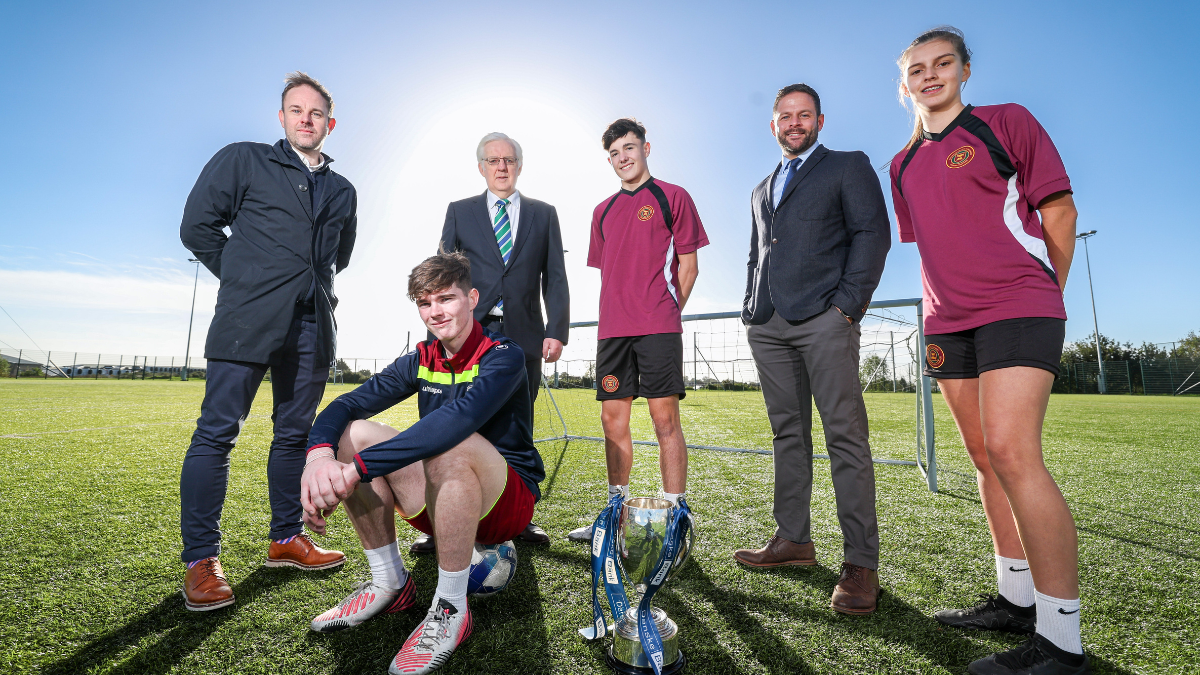 Six people stand outside on a football pitch. Three players from Dungannon Inegrated Colleage and three adults from Danske Bank and NISFA.