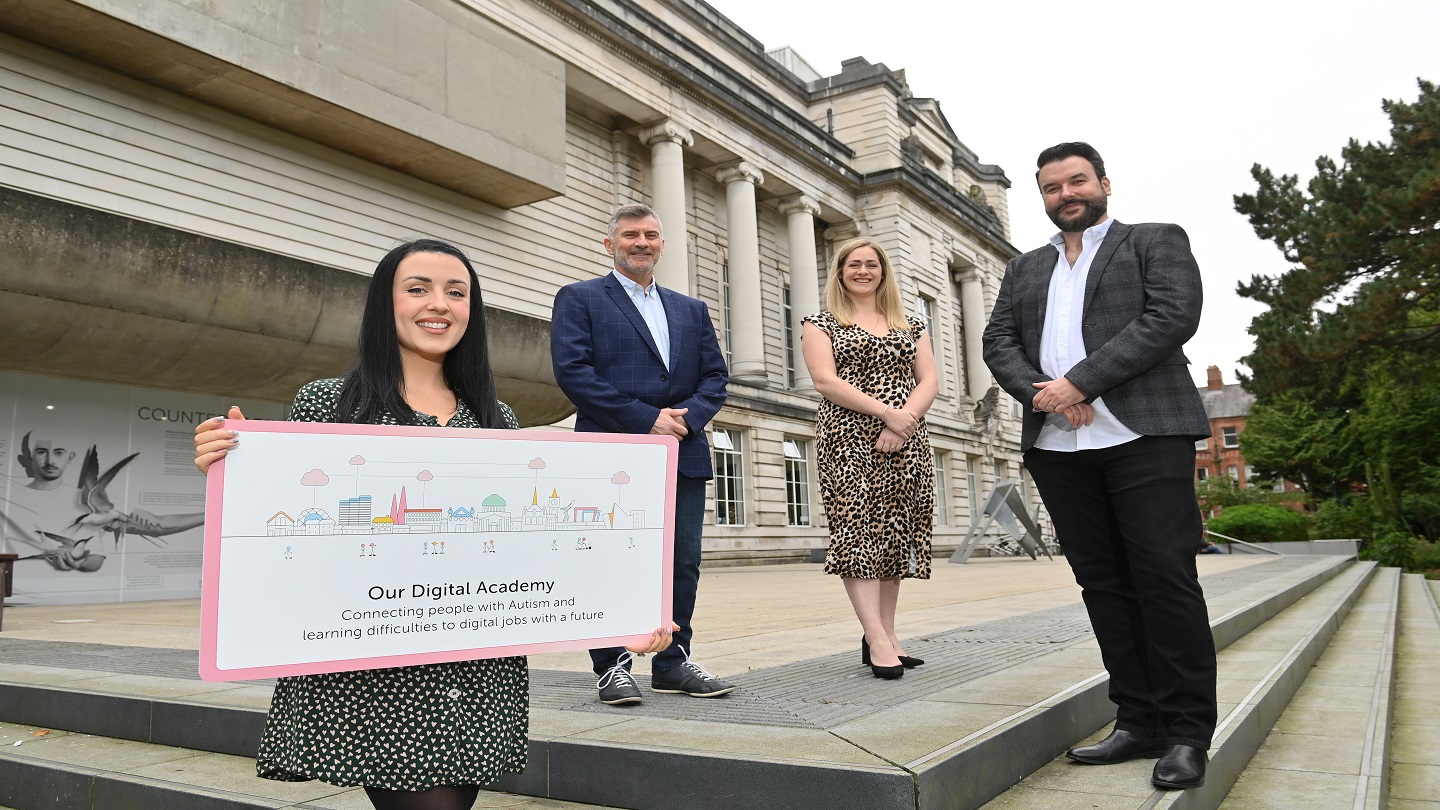 Image shows four people standing outside, at the front someone holds a sign about the digital academy.