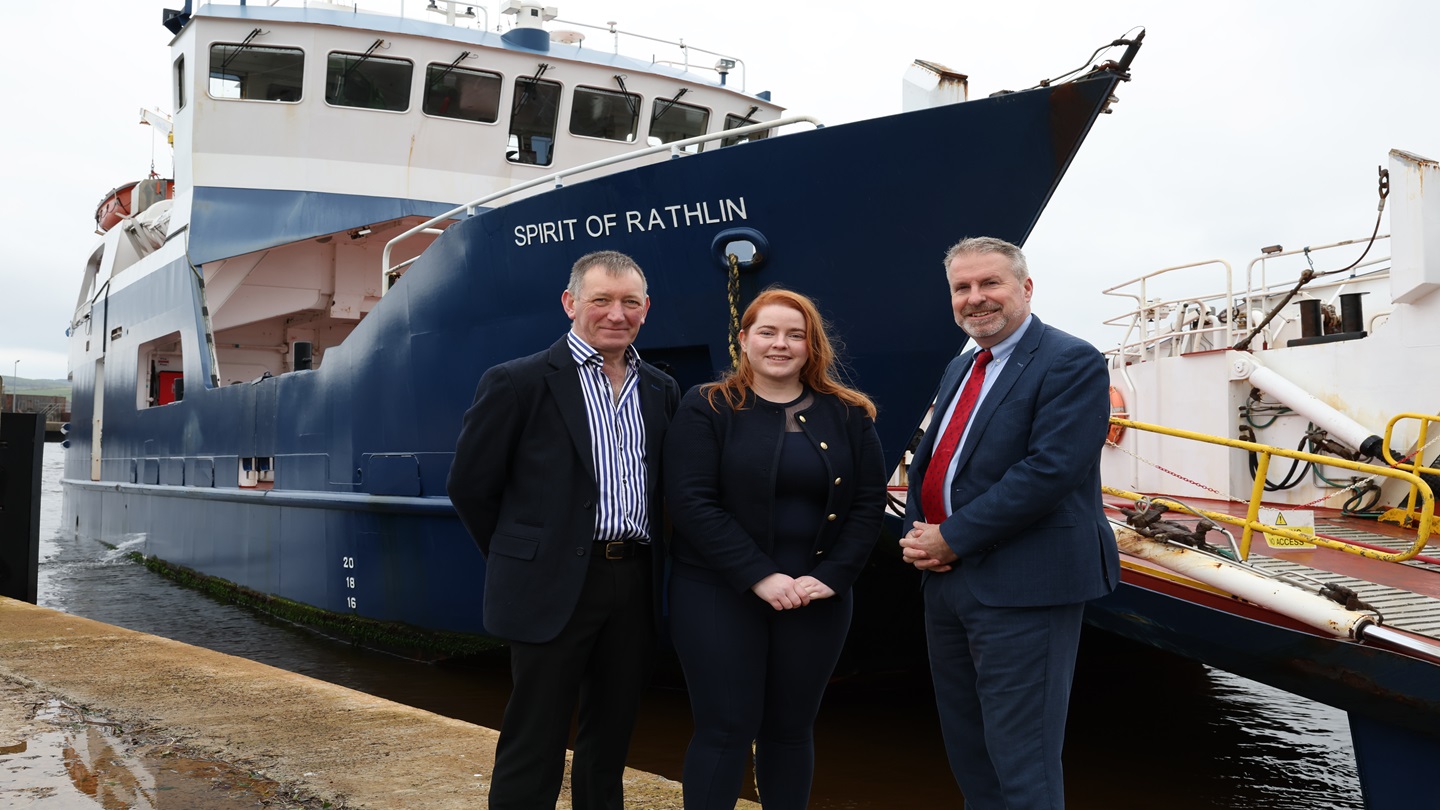 Three people pictured at a harbour. Behind them is a ferry boat called 'Spirit of Rathlin'