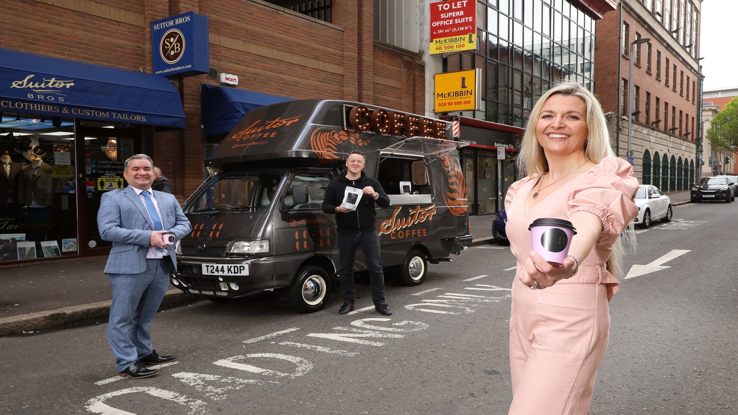 Three people standing outside - one is holding a coffee cup and one a bag of coffee beans, and behind them is a branded coffee van called 'Suitor Coffee'