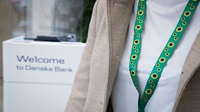 A close up of a person's torso - they are wearing a green lanyard with sunflowers printed on it. They are in a Danske Bank branch, with a 'Welcome to Danske Bank' stand behind them.