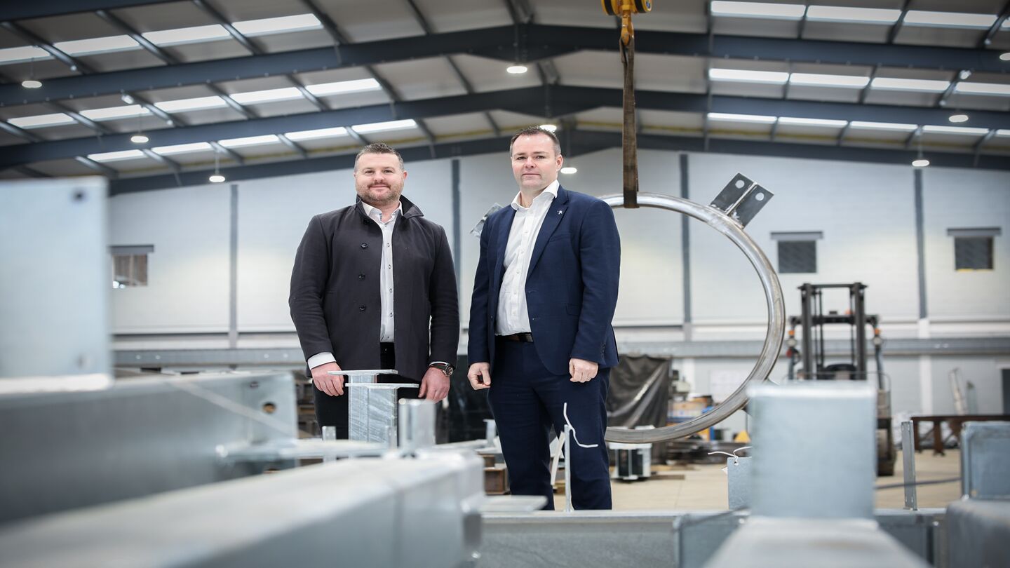 Two men stand inside a steel manufacturing factory