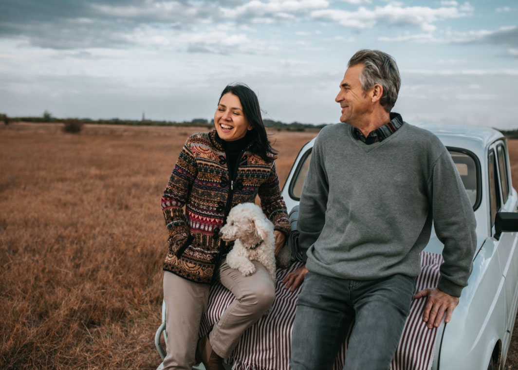 Man and woman sitting on bonnet of classic car with a dog